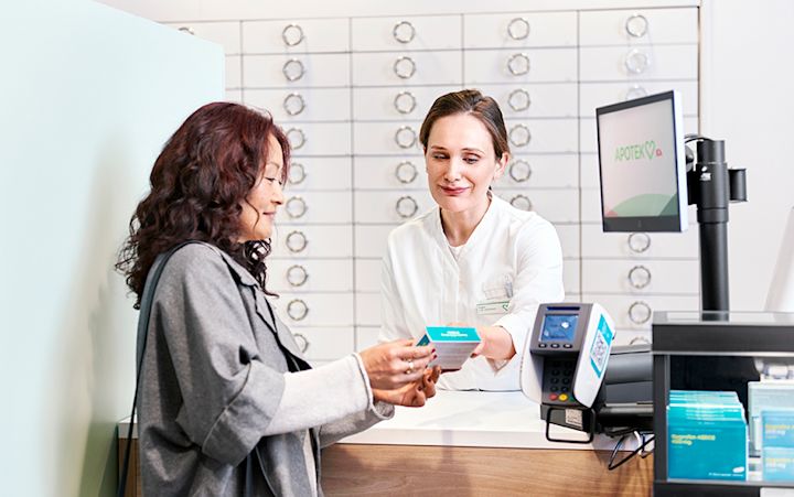 En kund står vid kassan och får rådgivning av en farmaceut.