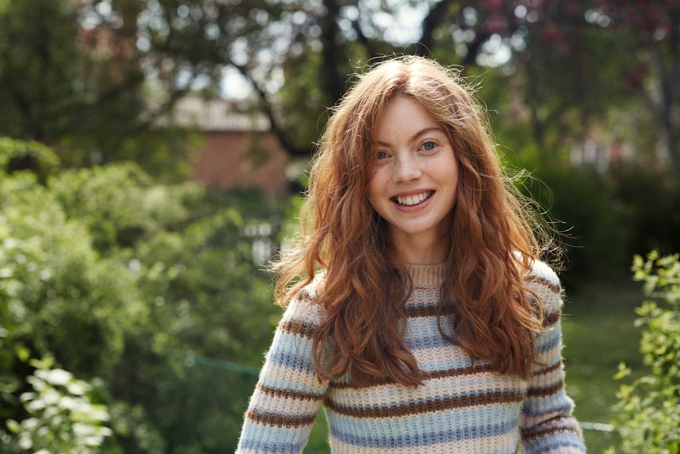 Tonårstjej står utomhus i trädgården och ler.