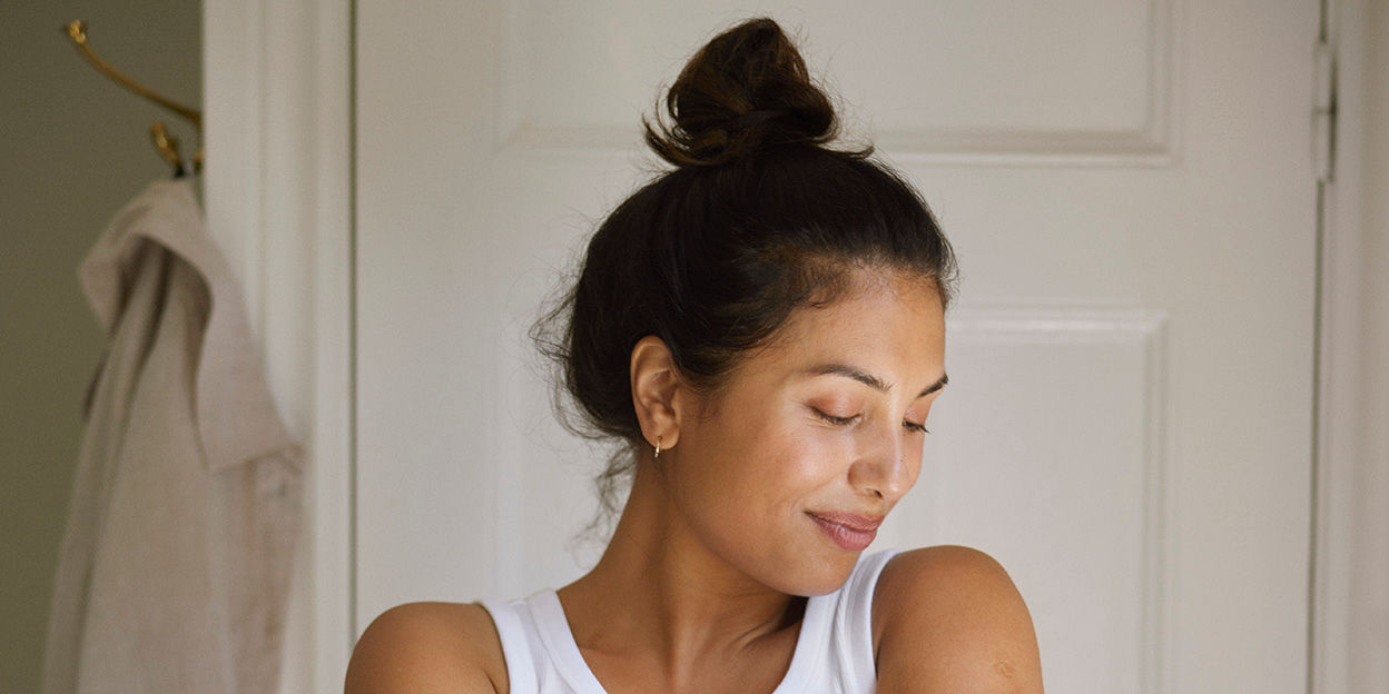 Kvinna med uppsatt hår står rakt fram kameran. Kollar snett nedåt. 