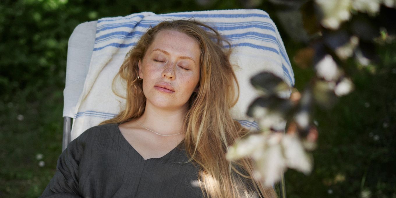 Kvinna sitter i solstol utomhus i skuggan och blundar.