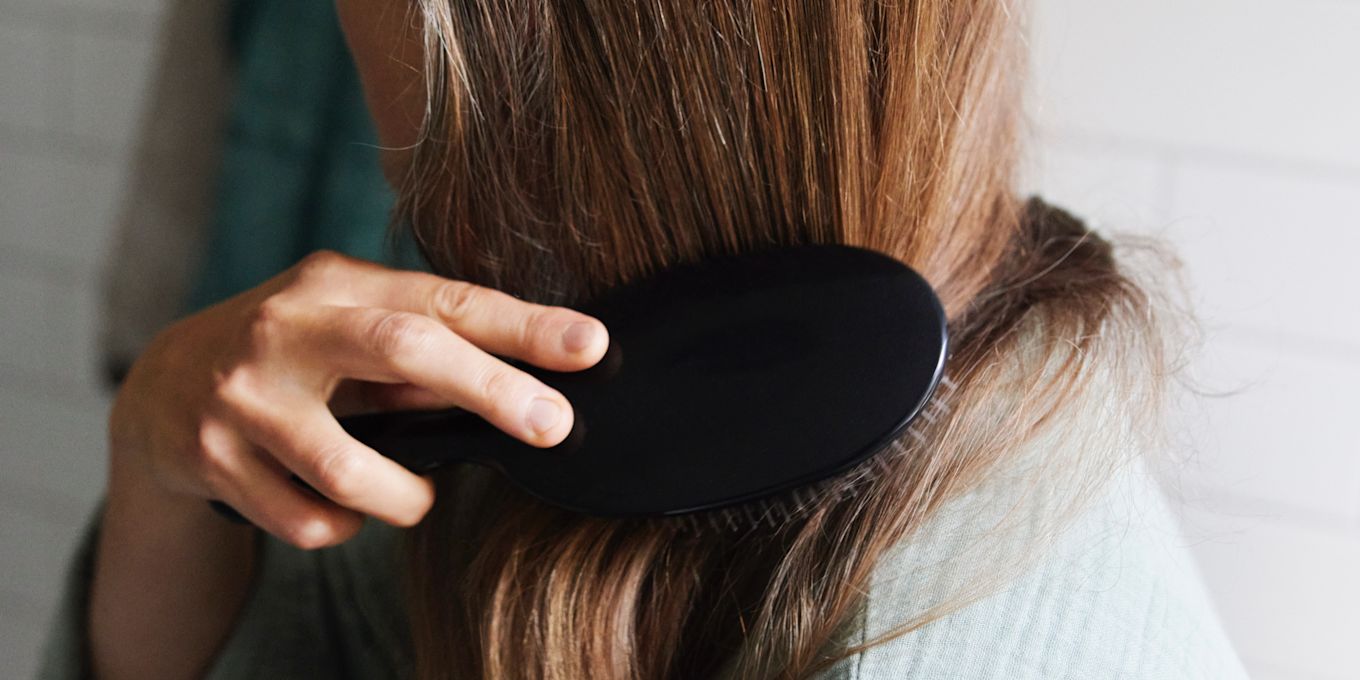 Kvinna som borstar sitt hår med en svart hårborste.
