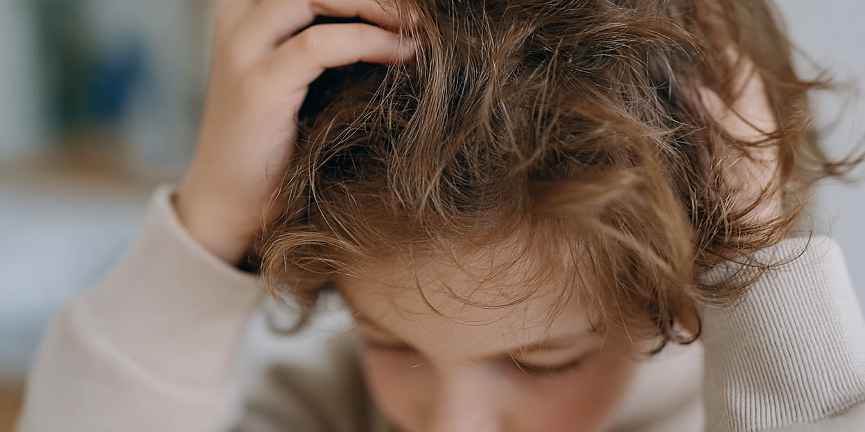 Pojke kliar sig i sitt halvlånga, lockiga och bruna hår. Bilden är delvis skapad med hjälp av AI.
