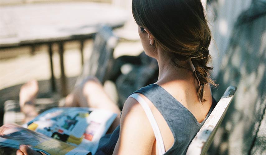 Kvinna sitter utomhus i en solstol och läser en tidning.