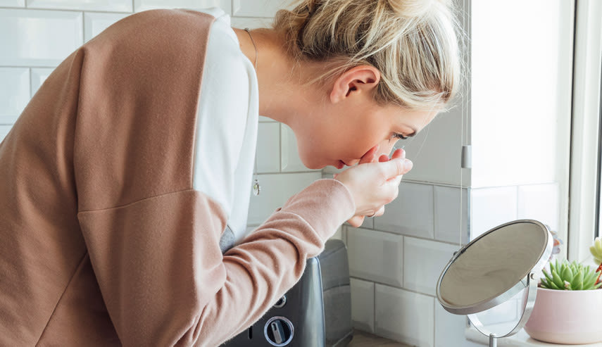 Kvinna i badrummet sätter i en kontaktlins i ögat och lutar sig fram över en spegel.