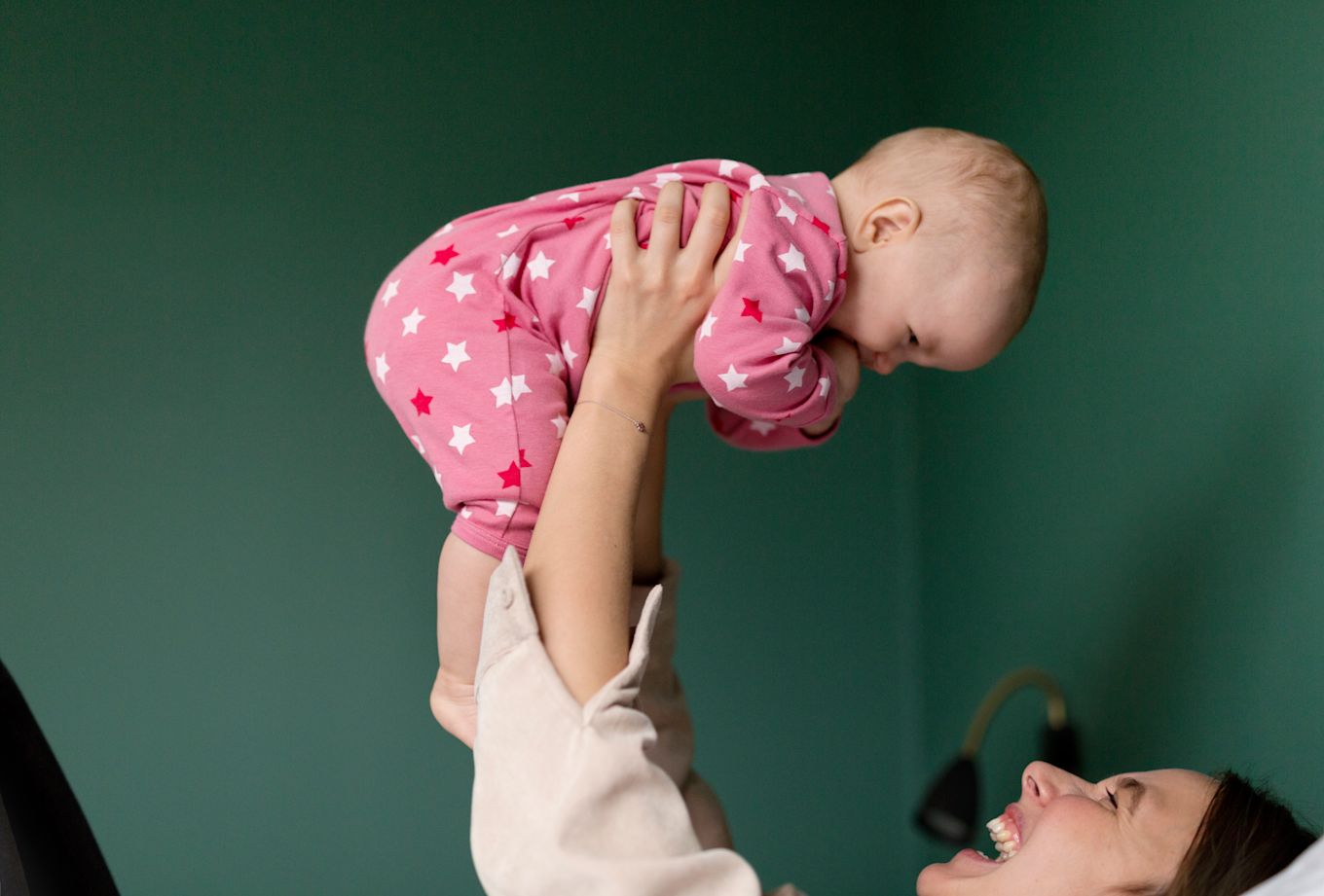 Mamma lyfter upp och leker med bebis i rosa sparkdräkt.