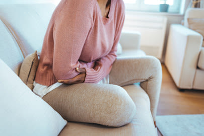 Kvinna sitter i soffan och håller om sin mage.