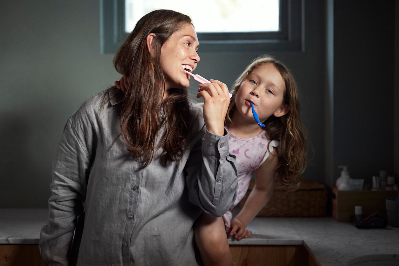 Mamma och dotter som står i badrummet och borstar tänderna.