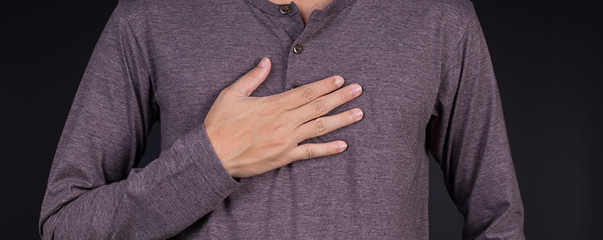 En person i en grå långärmad skjorta lägger sin högra hand på bröstet mot en mörk bakgrund.