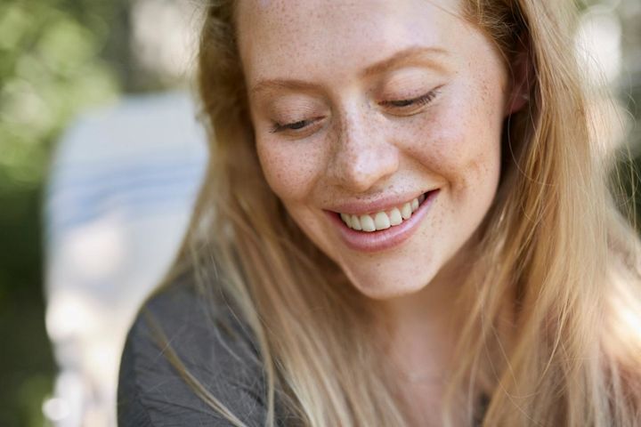 Kvinna ute i solen som tittar ner och ler.