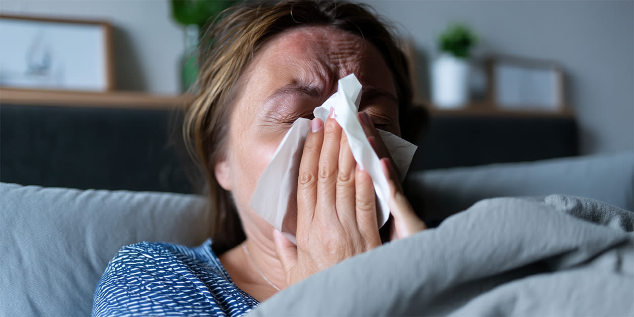 Kvinna sitter i soffan och snyter sig med en vit näsduk.