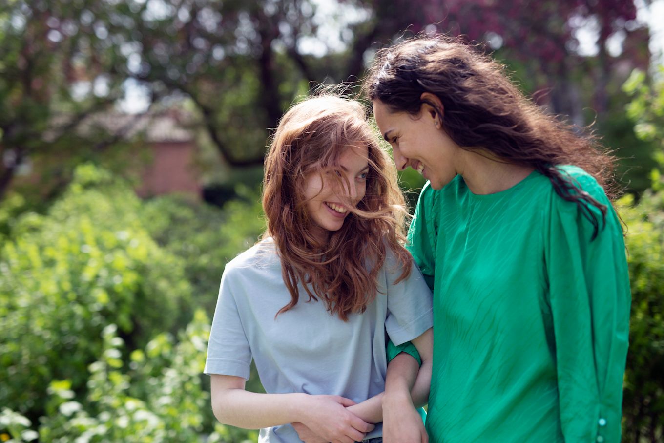 Mamma och tonårsdotter går utomhus arm i arm och pratar och skrattar.