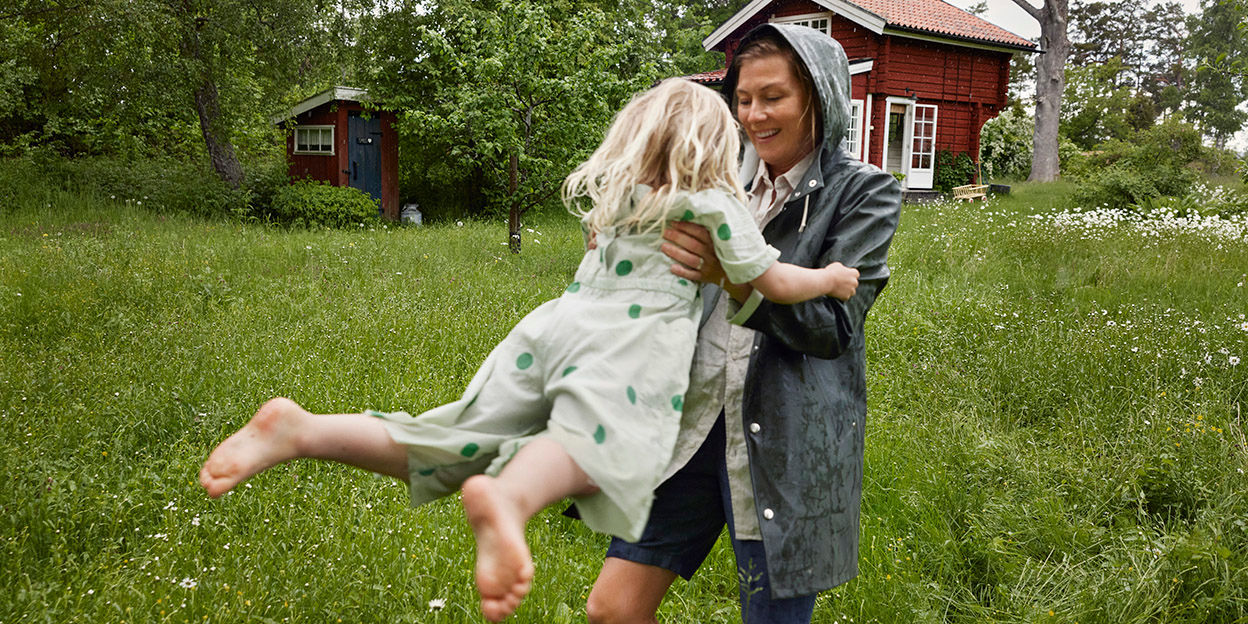 Kvinna håller lyfter barn och snurrar henne i en trädgård. 