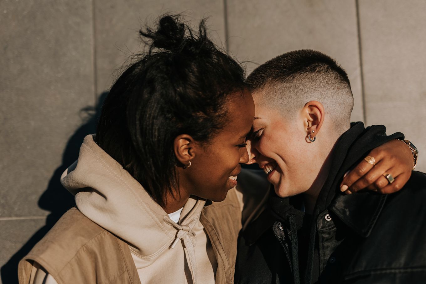 Två tonårstjejer står utomhus och kramar om varandra, ler och pussas.