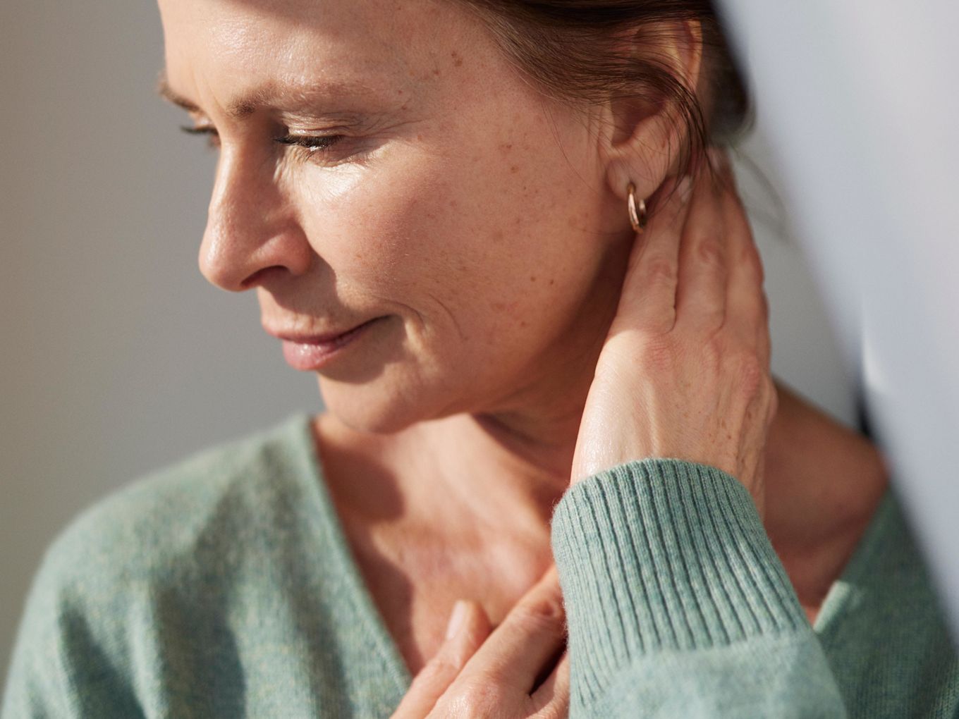 Kvinna tittar åt sidan, håller upp ena handen mot sin nacke.