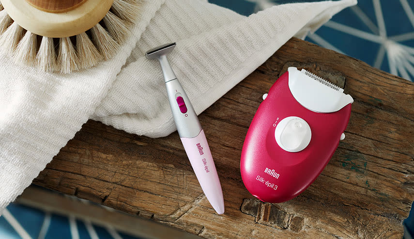 Två epilator-verktyg från Braun ligger vid en vit handduk i ett badrum.