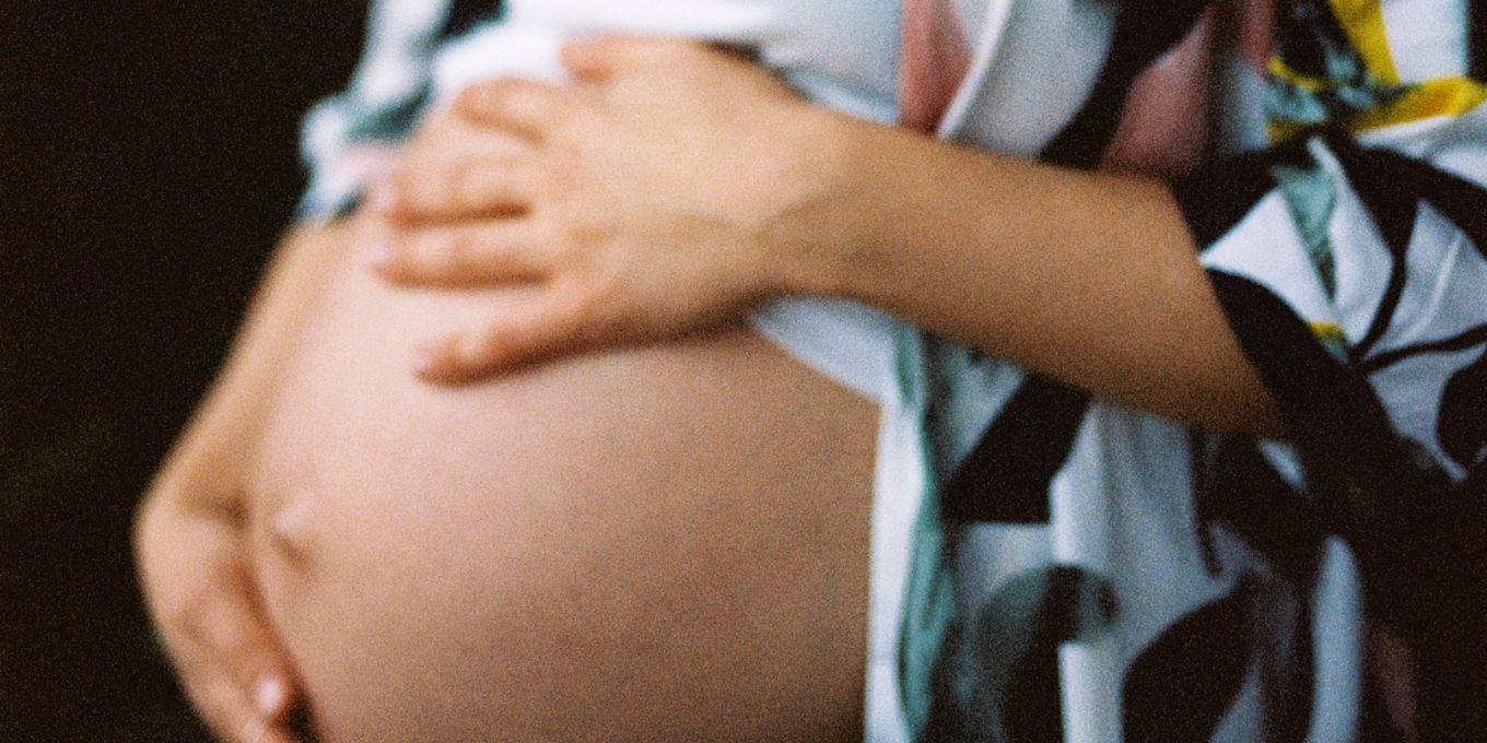 En gravid kvinna står och håller händerna på sin bara mage.