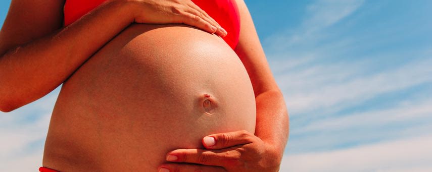 En närbild av en gravid kvinnas mage mot en klarblå himmel.