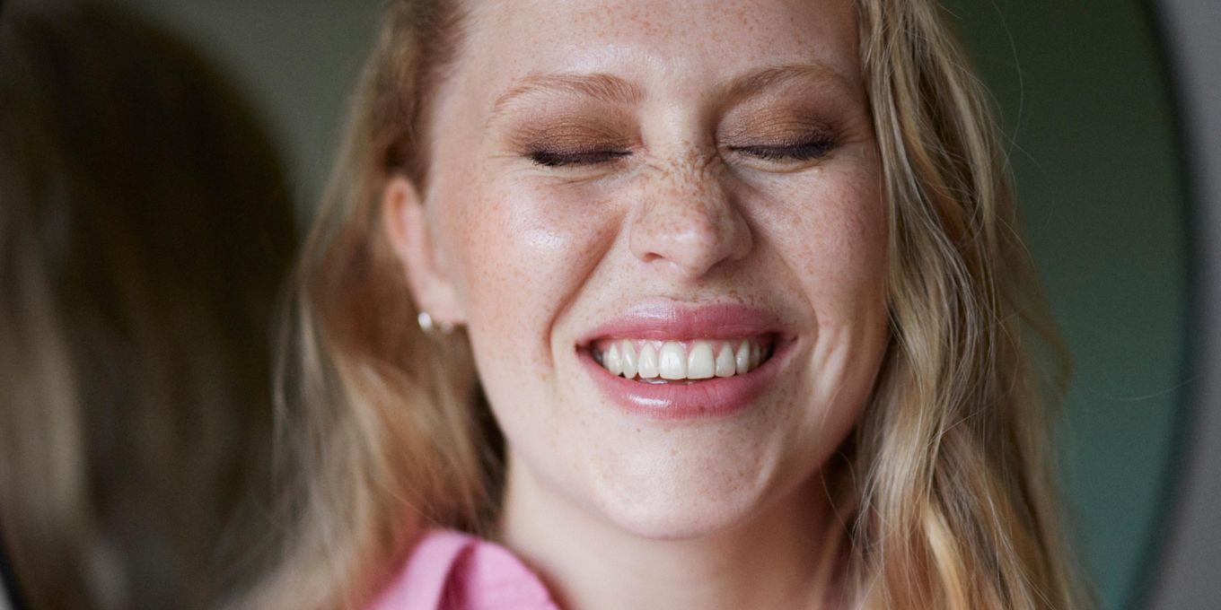Sminkad kvinna ler och kniper ihop ögonen.