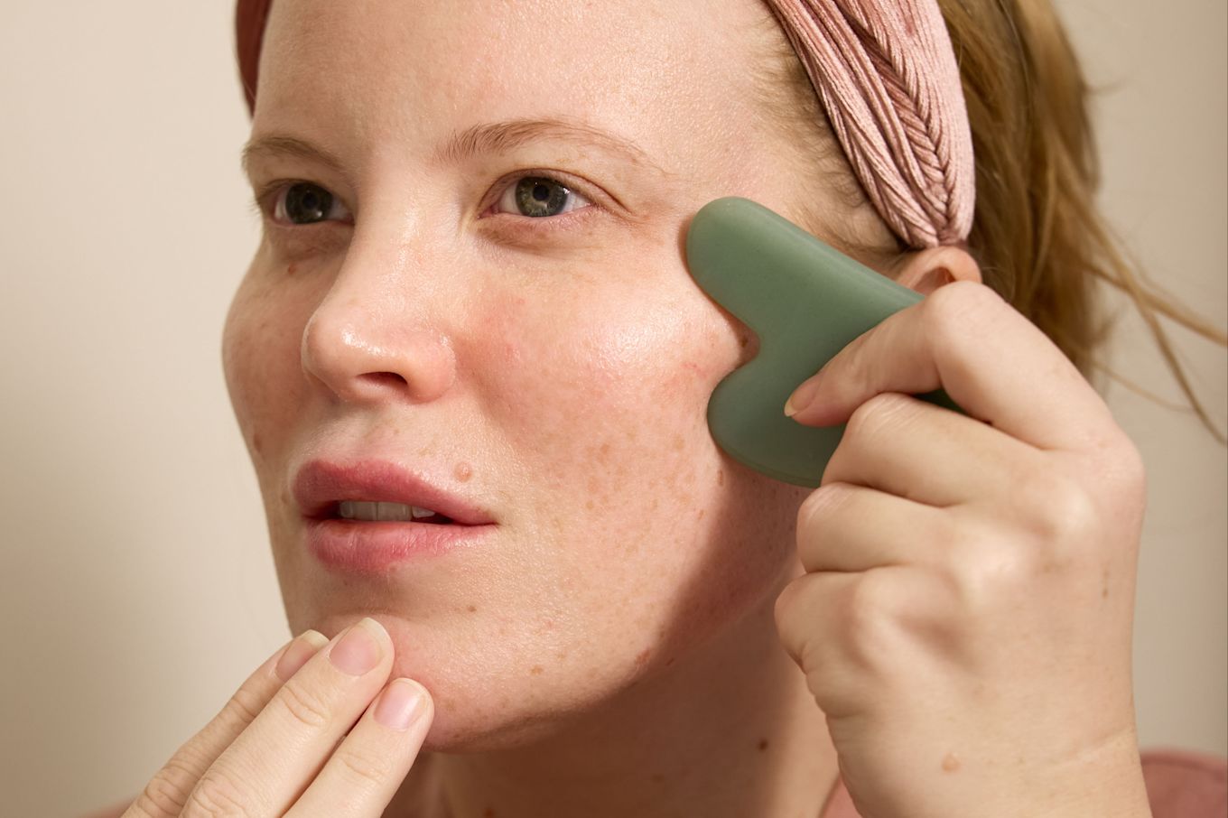 Tjej gör ansiktsyoga med en gua sha sten. Hon håller fingrarna på hakan och drar gua shan på kinden.