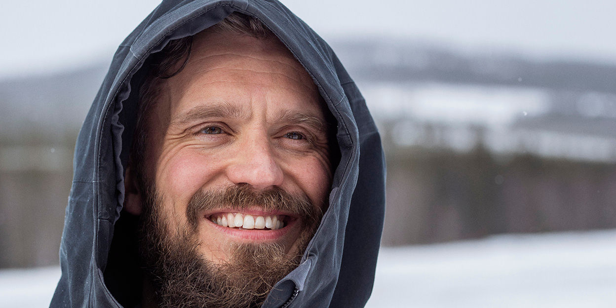 Skäggig man står utomhus och ler under vintern. 