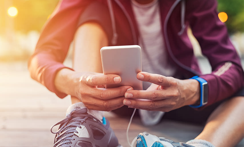 En person sitter och stretchar på marken och tittar i sin mobil.