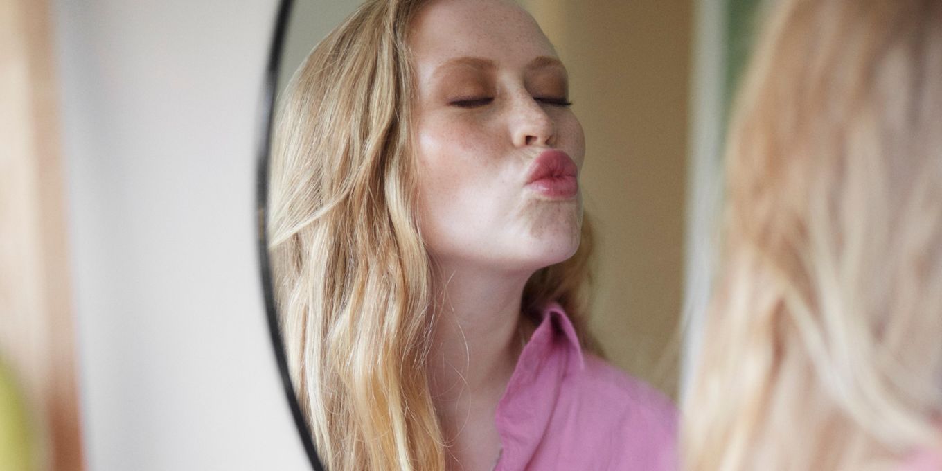 Sminkad kvinna speglar sig och gör pussmun mot sin reflektion.