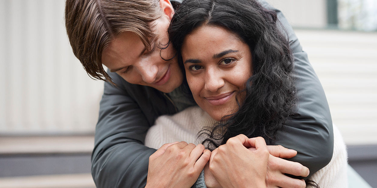 En kille kramar om en tjej. Tjejen kollar rätt in i kameran.