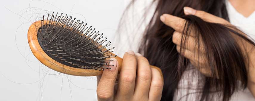 En kvinna tittar på sin hårborste, som är full av hår.